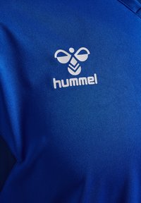Blaues Polyester-Sportshirt mit einem weißen Hummel-Logo und glatter Textur, mit einem dezenten Glanz und atmungsaktivem Design.