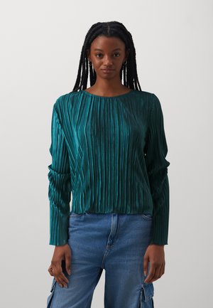 Teal plooien blouse met lange mouwen en een ronde halslijn, gemaakt van glanzende stof, gecombineerd met lichtblauwe high-waisted jeans.