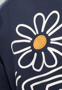 Navy t-shirt featuring a large white daisy graphic, with a textured yellow center and curved lines, made from soft cotton fabric.