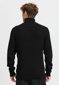 Suéter negro de punto con un patrón texturizado, cuello alto y puños y dobladillo acanalados. Diseñado para una silueta ajustada.