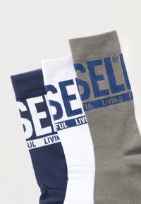 Drei Paar Socken: marineblau, weiß und grau. Jede hat ein auffälliges, gedrucktes Logo und Text in kontrastierenden Farben an den Bündchen.