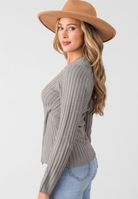 Maglione grigio a coste con maniche lunghe, caratterizzato da un collo a V e una vestibilità leggermente corta. Modella che indossa un cappello di paglia a tesa larga color sabbia.