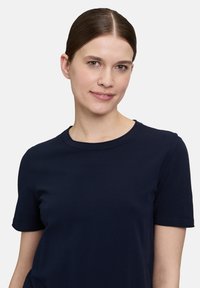 T-shirt en coton bleu marine avec un col rond, des manches courtes et une coupe décontractée. Texture lisse, sans motifs ni embellissements visibles.