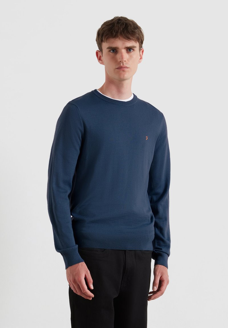 Granatowy sweter z dzianiny z długimi rękawami, okrągłym dekoltem i ribbowymi mankietami. Posiada małe logo na lewej piersi.