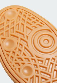 Rubber sole in soft orange with intricate geometric patterns, including circles and lines, providing traction and texture.