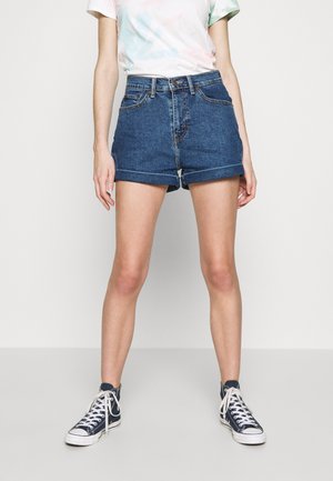 Shorts en denim, taille haute, bleu foncé, texture du tissu visible, ourlets roulés, associés à des baskets montantes navy, lacets blancs, style décontracté.