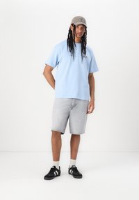 Lyseblå t-shirt med korte ærmer, grå denim shorts, sorte sneakers med hvide striber og en grå kasket. Enkel design, blød tekstur.