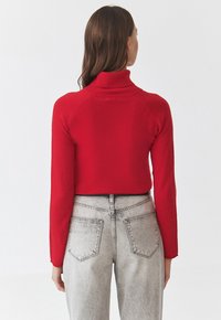Pulover roșu cu gât înalt, cu mâneci lungi, design ajustat și scurt, fabricat dintr-un material moale. Purtați-l peste blugi gri deschis cu talie înaltă, care au buzunare la spate.