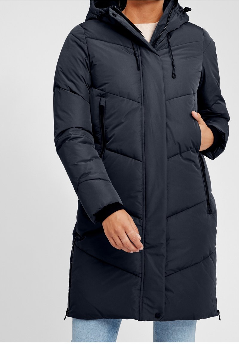 Padded kabát v tmavě námořnické barvě se zipem vepředu, kapucí na stahování, bočními kapsami a elastickými manžetami. Obsahuje diagonální šití pro strukturu.