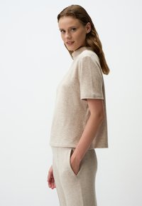 Top corto a maniche corte beige chiaro con colletto alto, realizzato in un morbido tessuto testurizzato, abbinato a pantaloni coordinati con tasche laterali.