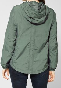 Lehká zelená bunda s kapucí, s detaily z prodyšné síťoviny na ramenou a bocích, elastickými manžetami a volným střihem.