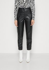 Svarta byxor i imitationsläder med en åtsittande design, hög midja och framfickor. Bärs med en långärmad randig topp och vita ankelskor.