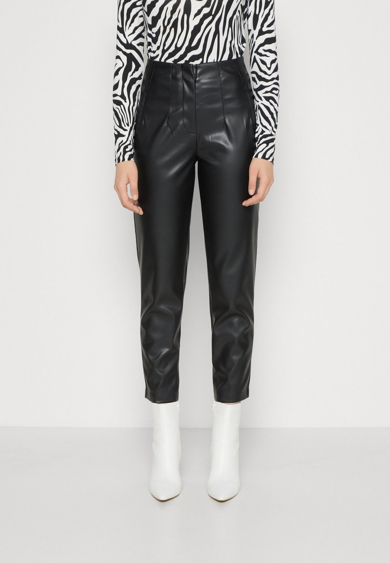 Svarta byxor i imitationsläder med en åtsittande design, hög midja och framfickor. Bärs med en långärmad randig topp och vita ankelskor.