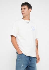 Witte katoenen t-shirt met korte mouwen, met een blauw tekstontwerp op de borst, gecombineerd met versleten lichtblauwe denim jeans.