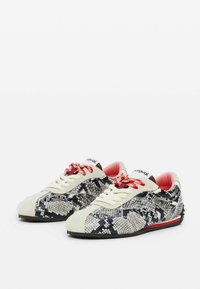 Sneakers mit einem Schlangendruckmuster in Grau-, Schwarz- und Cremetönen; verfügen über rote Schnürsenkel, ein rosa Innenfutter und eine strukturierte Sohle.
