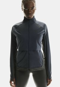 Veste de sport navy à manches longues, avec fermeture éclair à l'avant et texture contrastante. Présente une coupe ajustée, un léger éclat et un logo sur la poitrine.