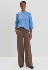 Helleblaue gerippte Strickjacke mit hohem Kragen und Dreiviertelärmeln, kombiniert mit hochtaillierten, braunen weiten Hosen und schwarzen Schuhen.