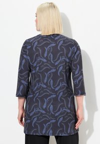 Tunic scura con maniche 3/4, caratterizzata da un motivo di foglie blu su sfondo nero. Texture liscia, taglio dritto, scende oltre i fianchi.