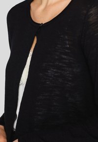 Svart kardigan i lätt, texturerat stickat med rund hals och en enda knapp fram.