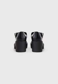 Black leather platform shoes with adjustable ankle straps and textured soles, featuring a round toe and solid block heels.