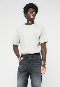 Grå kortermet t-skjorte kombinert med mørkegrå jeans. Stoffet er glatt med en avslappet passform, og har en klassisk rund hals.