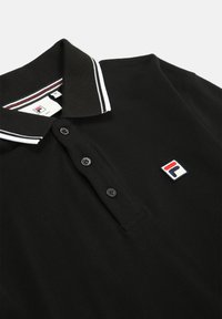 Camisa polo negra hecha de tela texturizada, con un cuello a rayas blancas, tres botones y un parche de logo multicolor en el pecho.