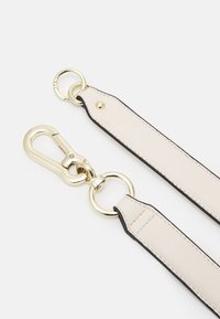 Beige kožený pásek s černými okraji, se zlatými kovovými doplňky, včetně klipu a dvou kulatých kroužků. Hladká textura, minimalistický design.