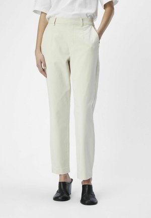 Pantalones ajustados beige claro con una cintura alta, bolsillos laterales y un corte slim. Combinados con mule de tacón bloque negro de punta abierta.