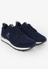 Marineblauwe sneakers van een combinatie van suede en mesh materialen. Voorzien van een doodskop en kruisbotten logo, witte zool en platte veters.