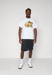 Valge puuvillane t-särk mitmevärvilise graafilise kujundusega, kombineeritud mustade lühikestega. Modell kannab valgeid tossusid ja pahkluusukke.