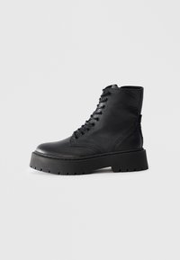 Bota de combate de cuero negro con suela gruesa de taco y cordones, mostrada en perfil lateral sobre un fondo blanco.