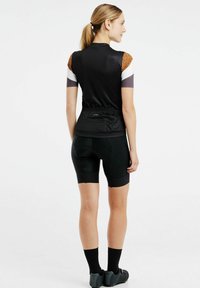 Maglia da ciclismo nera con maniche decorate, vita elastica posteriore, abbinata a pantaloni corti imbottiti neri e calzini e scarpe nere coordinate.