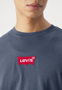 Granatowy t-shirt z okrągłym dekoltem i krótkimi rękawami, z wyhaftowanym na czerwono logo Levi's na piersi. Miękka, gładka textura materiału.