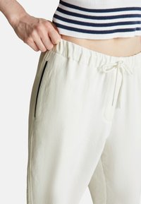 Bílé joggingové kalhoty s texturovaným povrchem, elastickým pasem, šňůrkovým zapínáním a bočními kapsami s černými akcenty.