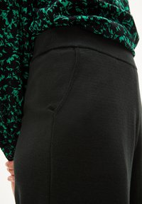 Zwarte joggingbroek van zacht materiaal, met een gladde tailleband en zijzak, gecombineerd met een gestreepte groene en zwarte top.