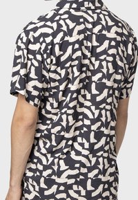 Camicia a maniche corte con uno sfondo blu navy e motivi astratti bianchi. Realizzata in un tessuto morbido, ha una vestibilità rilassata e colletto classico.