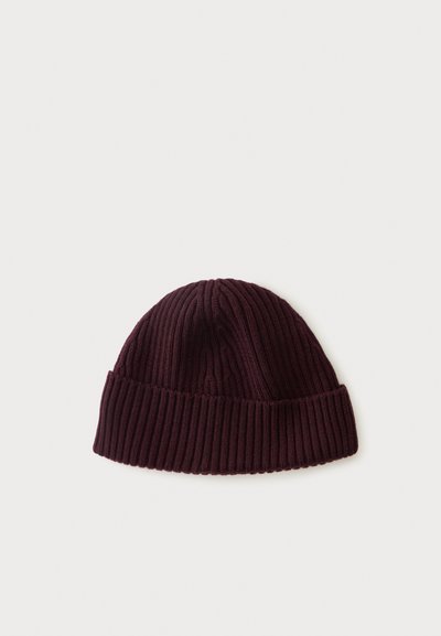 Bonnet en tricot côtelé violet foncé avec un revers sur un fond clair uni.