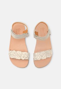Ljusbeiga sandaler med lädersula, utrustade med ett smalt vristband och en dekorativ, utskuren blommönsterdesign på den främre remmen.