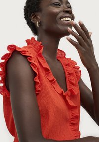 Rote Bluse mit Rüschensleeves, strukturierter Stoff, V-Ausschnitt und subtilen Falten, die lebendige Farben und eine dynamische Form zur Schau stellt.