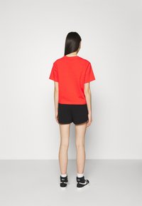 Red cropped t-shirt with short sleeves, paired with black shorts. The outfit features a simple design and is complemented by black sneakers.