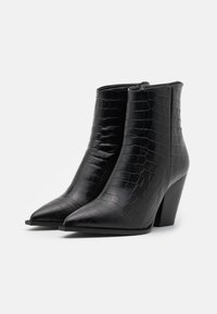 Bottines noires en simili cuir avec un motif croco, bout pointu et talon épais. Équipées d'une fermeture éclair sur le côté.