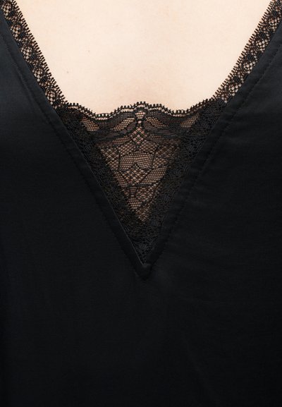 Μαύρο ένδυμα με λαιμόκοψη V και λεπτή δαντέλα με λουλουδένιο σχέδιο που καλύπτει την επιδερμίδα στο λαιμό.