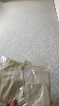 Beige kledingstuk met verticale strepen, gemaakt van lichtgewicht stof, gedeeltelijk zichtbaar in een doorzichtige plastic verpakking. Gelaagde, platte ondergrond.