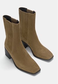 Bottines en daim marron avec un bout carré, des panneaux latéraux élastiques et un talon large noir. La texture est douce et le design est élégant.