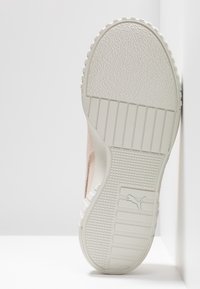 Semelle de chaussure de sport blanche avec motif de grip texturé, comportant un logo. Vue latérale avec une tige en matériau blanc cassé et rose clair.