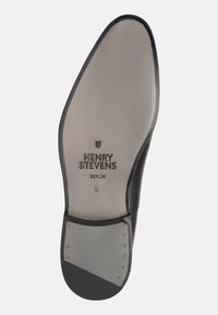 Semelle de chaussure en cuir noir avec une finition lisse, portant le texte gaufré "HENRY STEVENS BERLIN" et des accents en métal le long du bord.