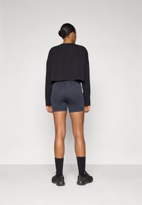 Felpa nera corta e pantaloncini biker grigio scuro, con texture del tessuto liscia e decorazioni minime, indossati con sneakers e calze nere.