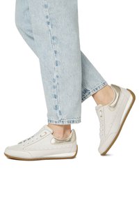 White sneakers with metallic gold accents, smooth leather upper, lace-up design, and rubber outsole; paired with light blue denim jeans.