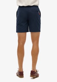 Pantalones cortos azul marino con una cintura elástica, bolsillos laterales y un bolsillo trasero con cremallera. Tela suave, hasta la rodilla, diseño minimalista.