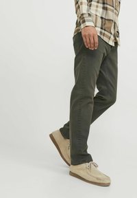 Pantalones verde oscuro de algodón, con un diseño ajustado. Combinados con zapatos de gamuza beige y una camisa de cuadros en tonos neutros.